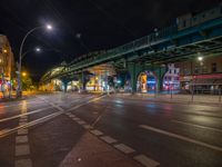 the empty street is filled with people walking and biking under an overpass at night