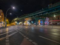 the empty street is filled with people walking and biking under an overpass at night