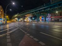 the empty street is filled with people walking and biking under an overpass at night