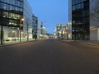 a paved street in the middle of buildings with tall windows at night, with car lights on