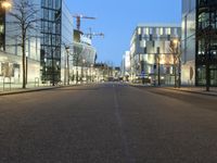 a paved street in the middle of buildings with tall windows at night, with car lights on