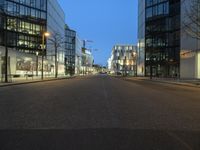 a paved street in the middle of buildings with tall windows at night, with car lights on