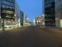 a paved street in the middle of buildings with tall windows at night, with car lights on