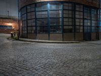 some dark blue windows in an industrial building with no one on the street to the right