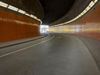 an empty road with a curved tunnel leading through it at night, which is a cyclist and a passenger in the distance