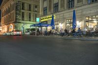 people sit on chairs at the outdoor cafe area in the city at night time, in front of a building