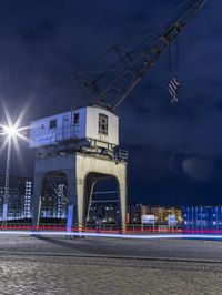 a night view of cranes and lights on a building with a car going by it