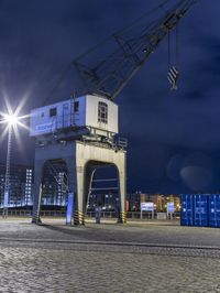 a night view of cranes and lights on a building with a car going by it