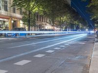 a street with cars passing by and a line of trees in the city during night