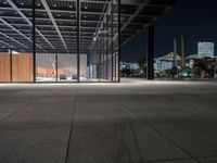 a large concrete covered outdoor walkway in the night time with city skylines behind it