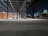 a large concrete covered outdoor walkway in the night time with city skylines behind it