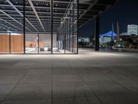 a large concrete covered outdoor walkway in the night time with city skylines behind it