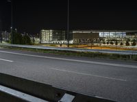 a bench sitting next to the side of a road in an empty parking lot at night