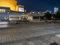 a building with a stairway next to it at night, in an empty plaza with lights shining off and buildings in the background