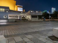 a building with a stairway next to it at night, in an empty plaza with lights shining off and buildings in the background