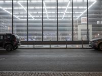 some cars and some buildings at night in a city street by windows at a parking structure