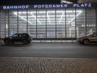 some cars and some buildings at night in a city street by windows at a parking structure