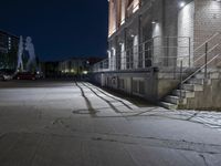 a person holding an umbrella standing on the sidewalk near stairs at night in an empty street