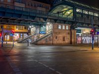 the empty street is filled with people walking and biking under an overpass at night