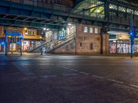 the empty street is filled with people walking and biking under an overpass at night