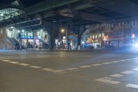 the night time view of a street under an overpass in tokyo, japan with people walking and cars driving at the traffic lights