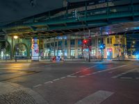 the empty street is filled with people walking and biking under an overpass at night