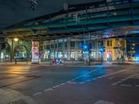 the empty street is filled with people walking and biking under an overpass at night