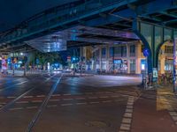 the empty street is filled with people walking and biking under an overpass at night