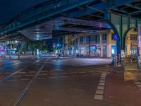 the empty street is filled with people walking and biking under an overpass at night