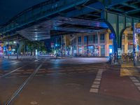 the empty street is filled with people walking and biking under an overpass at night