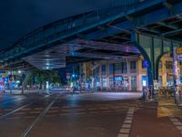 the empty street is filled with people walking and biking under an overpass at night