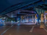 the empty street is filled with people walking and biking under an overpass at night