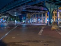 the empty street is filled with people walking and biking under an overpass at night