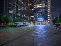 the night time image is lit from outside with buildings and street lights in it, at the end of the road