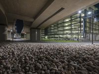 rocks cover a large sidewalk next to a building at night with lit up windows in the distance