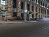 some benches on the side of a busy street near buildings with traffic passing by at night