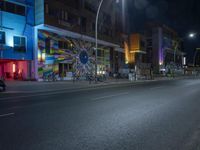 an empty street near some buildings in front of a street light at night with bright colors