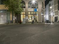 a building on the corner of an empty street at night time, next to cars and bicycle parking