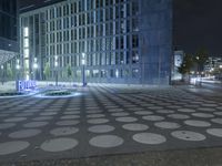 a clock sits on the ground outside of a large building at night, with blue light on it