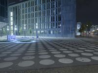 a clock sits on the ground outside of a large building at night, with blue light on it