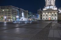 there are a few buildings next to each other in a square area with fountains at night