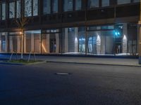 a person is standing on the sidewalk of a building at night as a traffic light illuminates