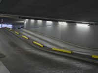 two yellow striped caution barriers in an empty parking garage at night time with cars going down an incline