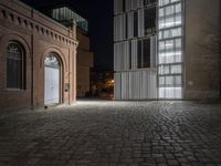 an empty brick walkway in front of some tall buildings at night time a large building is located next to a door