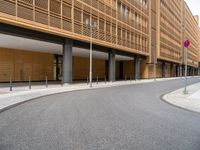 the empty street and entrance of an office building with balconies and trees on the side