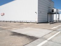 a large white warehouse building with windows on a sunny day in the parking lot for commercial and industrial vehicles