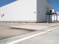 a large white warehouse building with windows on a sunny day in the parking lot for commercial and industrial vehicles