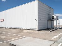 a large white warehouse building with windows on a sunny day in the parking lot for commercial and industrial vehicles