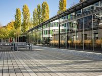 a glass office with trees reflected in the windows and the ground under the bench is paved