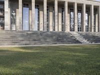 large, gray stone building with stairs going up to it and grass growing around the area